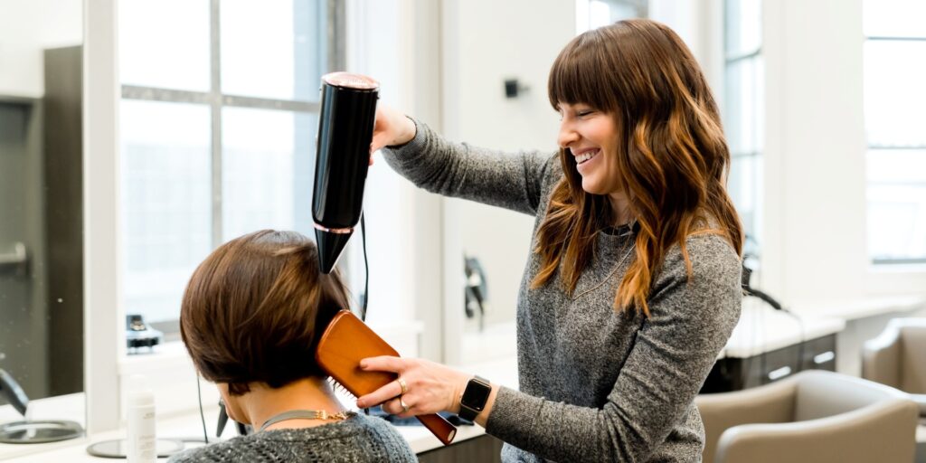 Eine Existenzgründerin eröffnet einen Friseursalon. Mit Werbung von "Sandra Hirsch Kommunikation und Training" wirbt sie neue Kundinnen und Kunden.